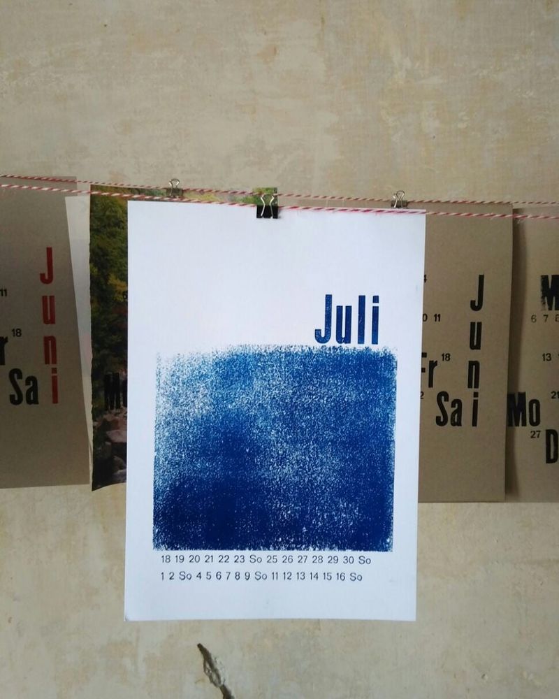 Kalenderblatt „Juli“ mit blau gedruckter Fläche, an einer Leine aufgehängt