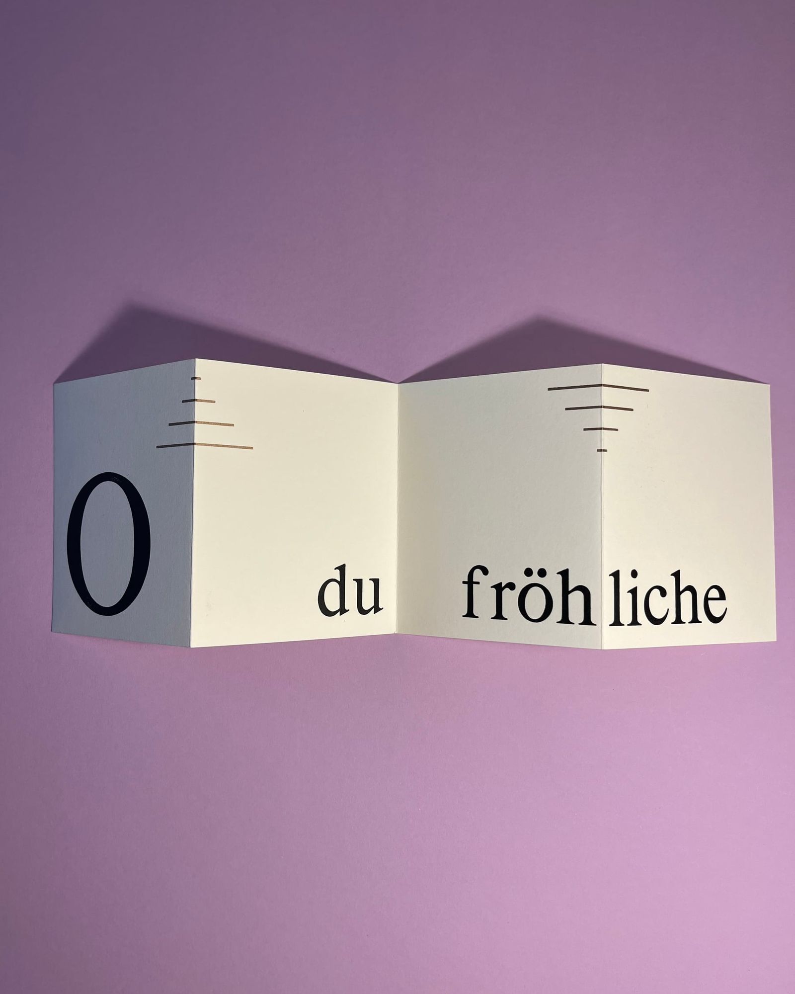 Aufgefaltetes Leporello „O du fröhliche“ vor violettem Hintergrund