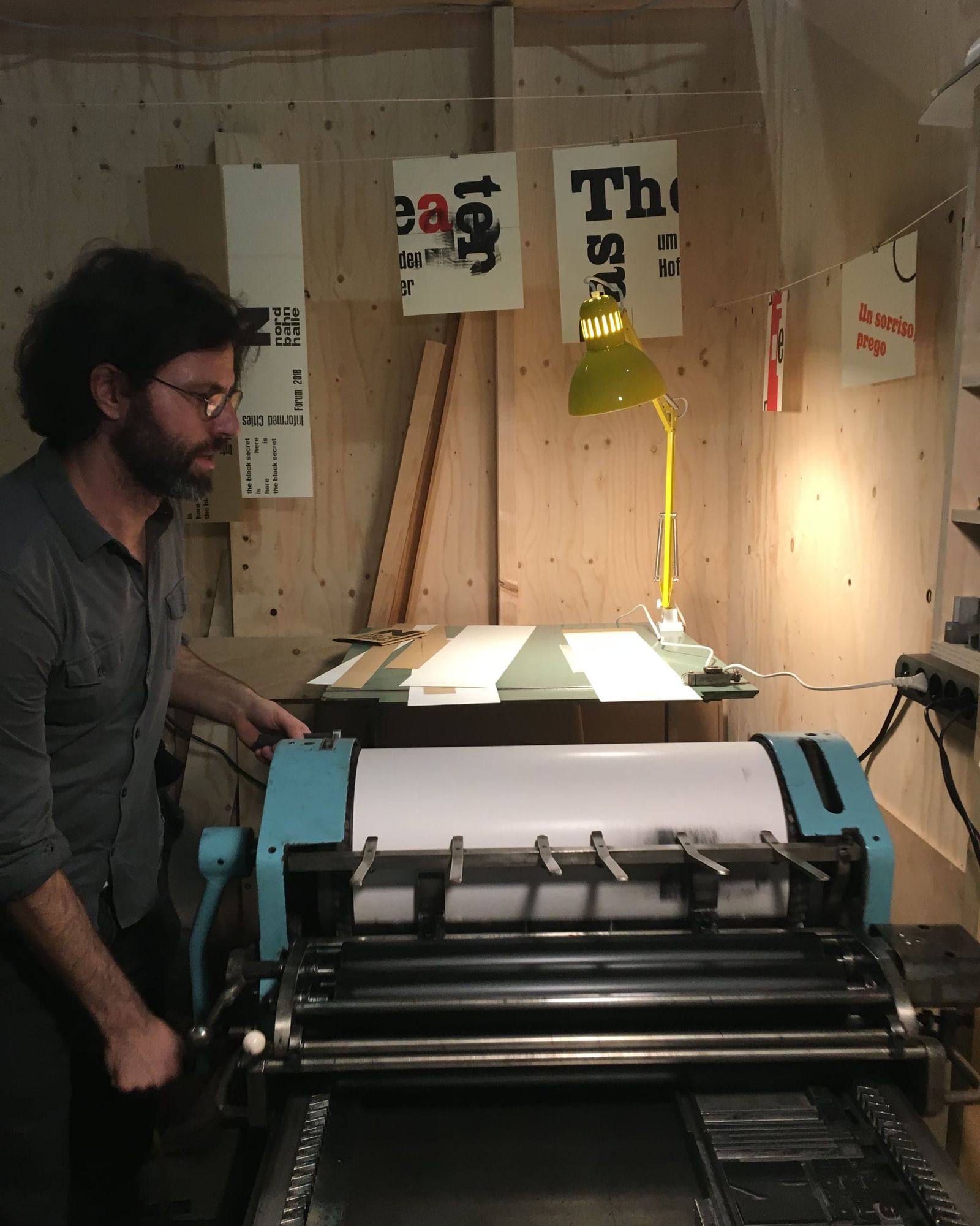 Alexander Zöhrer an der Druckmaschine, dahinter hängen frisch gedruckte Plakate